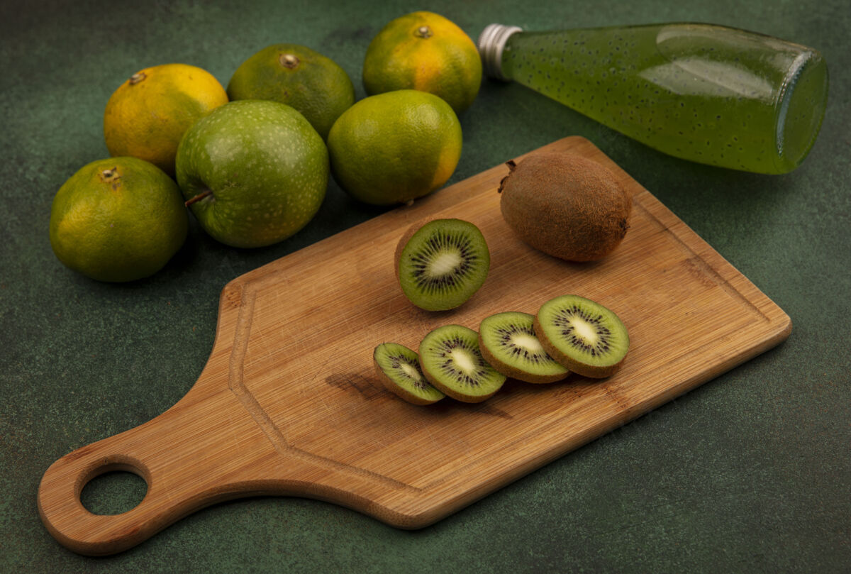 猕猴桃侧视图猕猴桃片在砧板上 橘子和一瓶果汁放在绿色的墙上木板视野食物