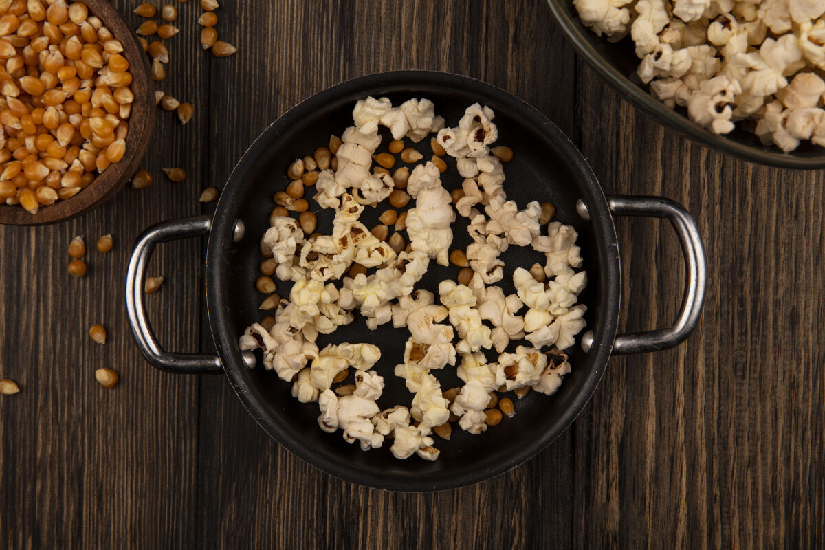 电影木墙上的木碗上放着爆米花和玉米粒的酱锅俯视图视图碗电影