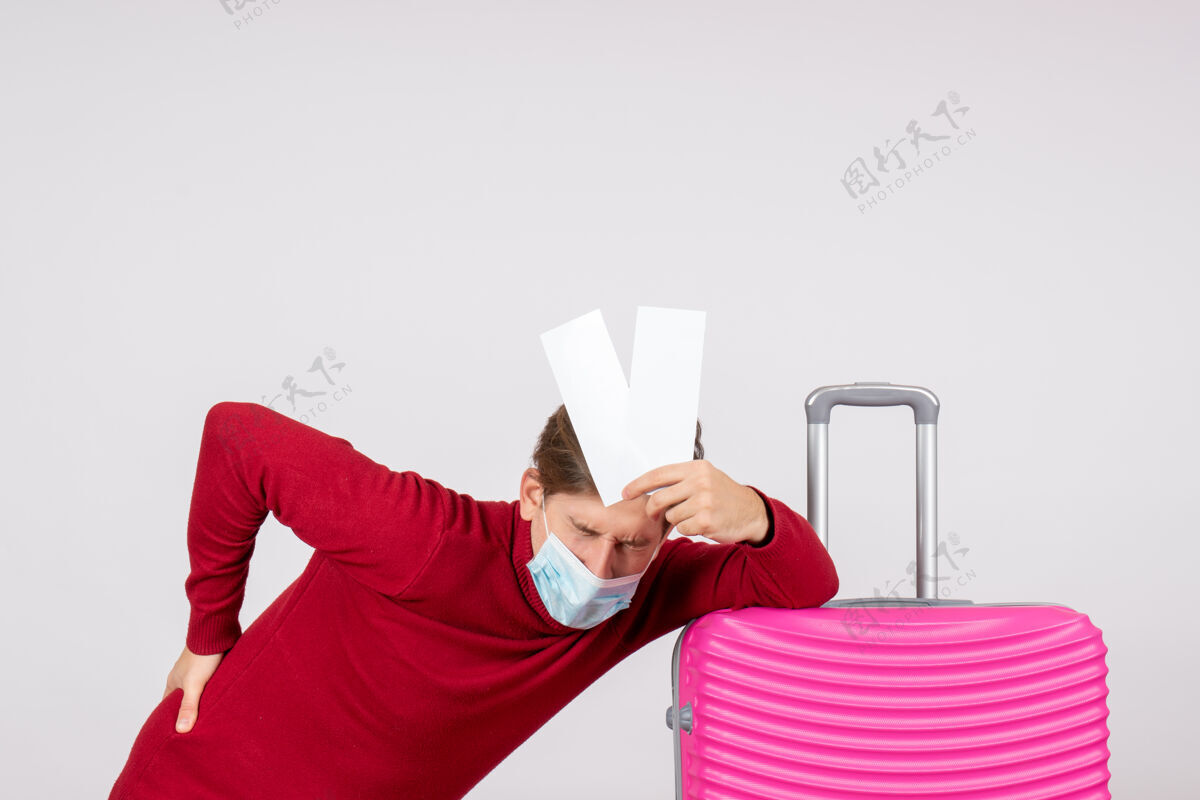 成人白墙上戴着面具拿着飞机票的年轻男子的正视图流行病前面旅行