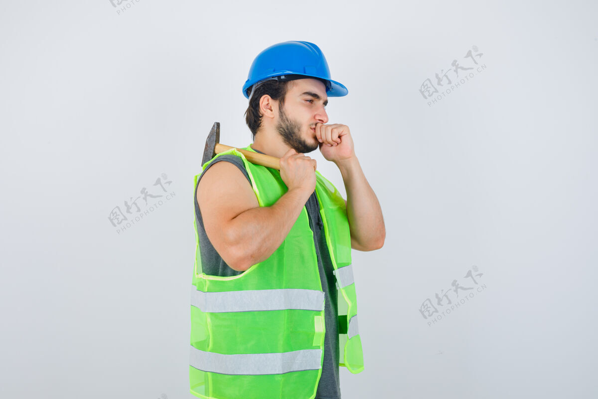 冬天年轻的建筑工人穿着工作服 肩上扛着锤子 嘴上紧握着拳头 神情沉思 俯视前方制服拳头锤子