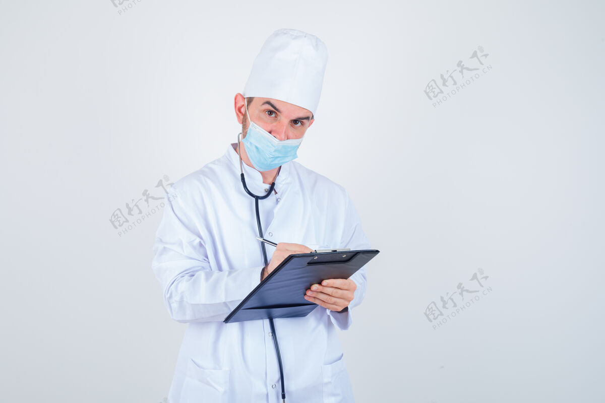 医院年轻的男医生穿着白色制服 戴着口罩 看上去很懂事 正对着剪贴板做笔记智能人士保健人员