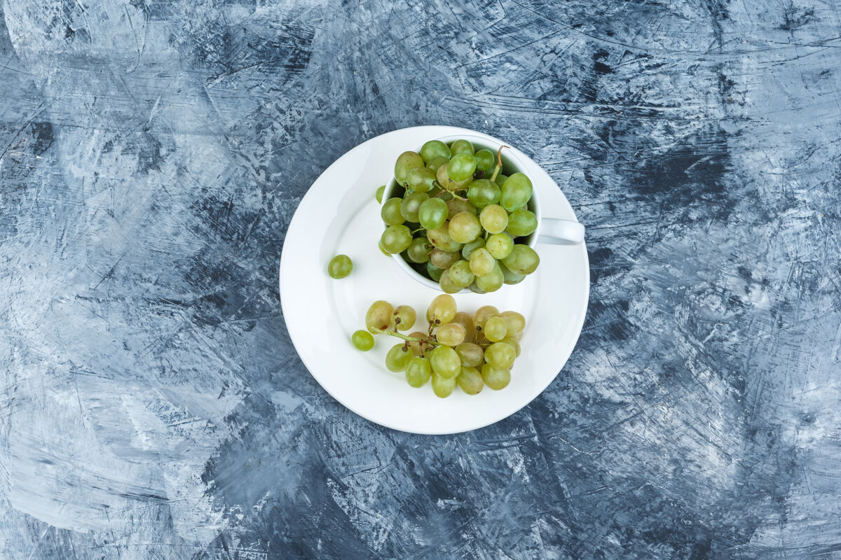 秋天绿色葡萄在白色的杯子和盘子顶视图上一个肮脏的石膏背景饮食光明藤