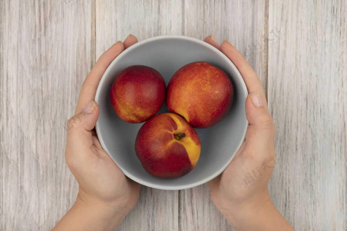 有机女性手拿着一碗新鲜甜桃子在灰色木头表面的俯视图饮食配料新鲜