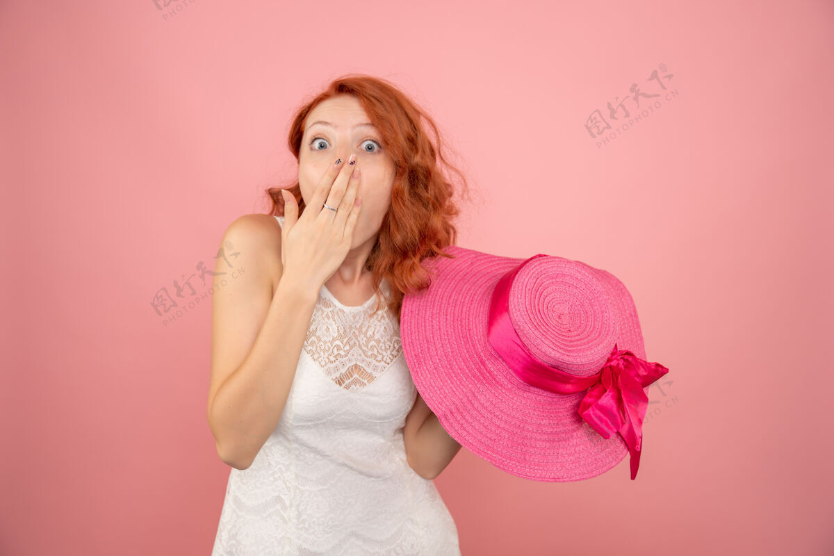 脸在粉红色的墙上戴着粉红色帽子的年轻女性的正视图年轻女性成人情绪