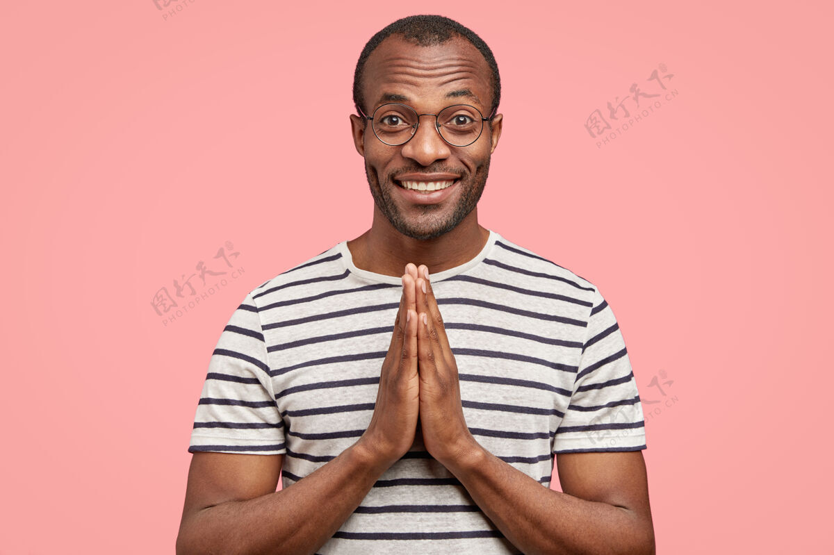 朋友室内拍摄的令人高兴的黑色黑皮肤男子保持双手祈祷的姿态健康未刮胡子精神