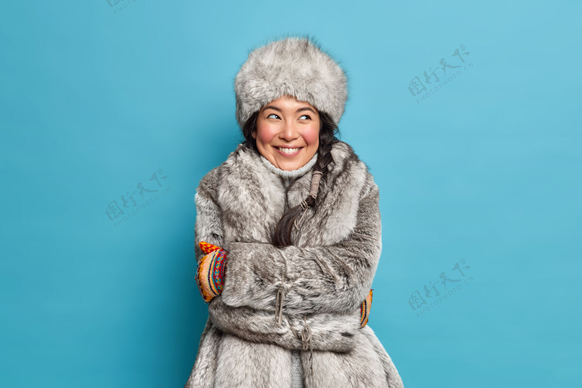 请可爱的爱斯基摩年轻女子拥抱着自己 穿着冬衣和帽子感觉很舒服 蓝色的墙壁上有着梦幻般的表情胭脂女性可爱