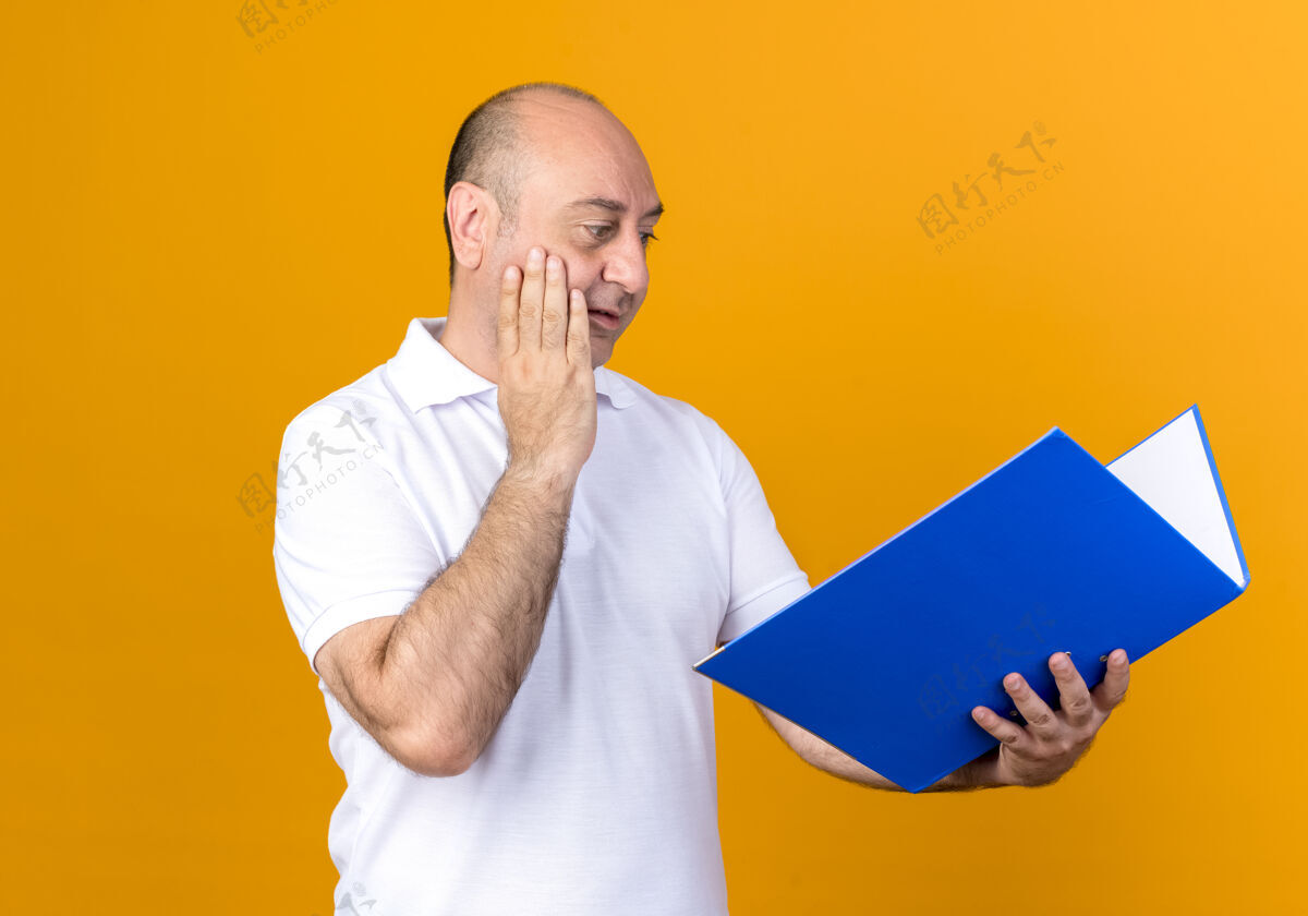 手意外的成熟男人不经意的拿着文件夹 看着文件夹 把手放在隔离在黄色墙上的脸颊上男人成熟夹