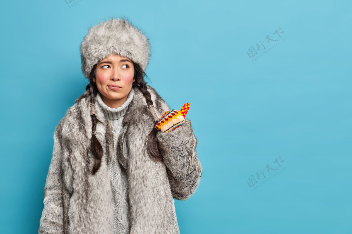 成人穿着传统冬装的不高兴的因纽特人女人看起来很不情愿 指着蓝色工作室墙上的空白处衣服不高兴传统