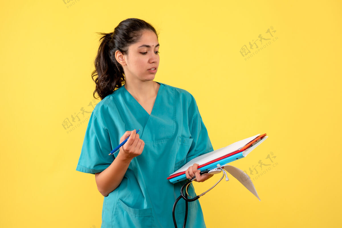 年轻女医生身着制服的年轻女医生站在黄色墙壁上检查文件的正面图护士检查纸