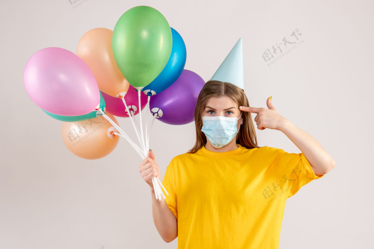 消毒年轻的女性手持彩色气球 戴着白色的无菌口罩举行大流行娱乐