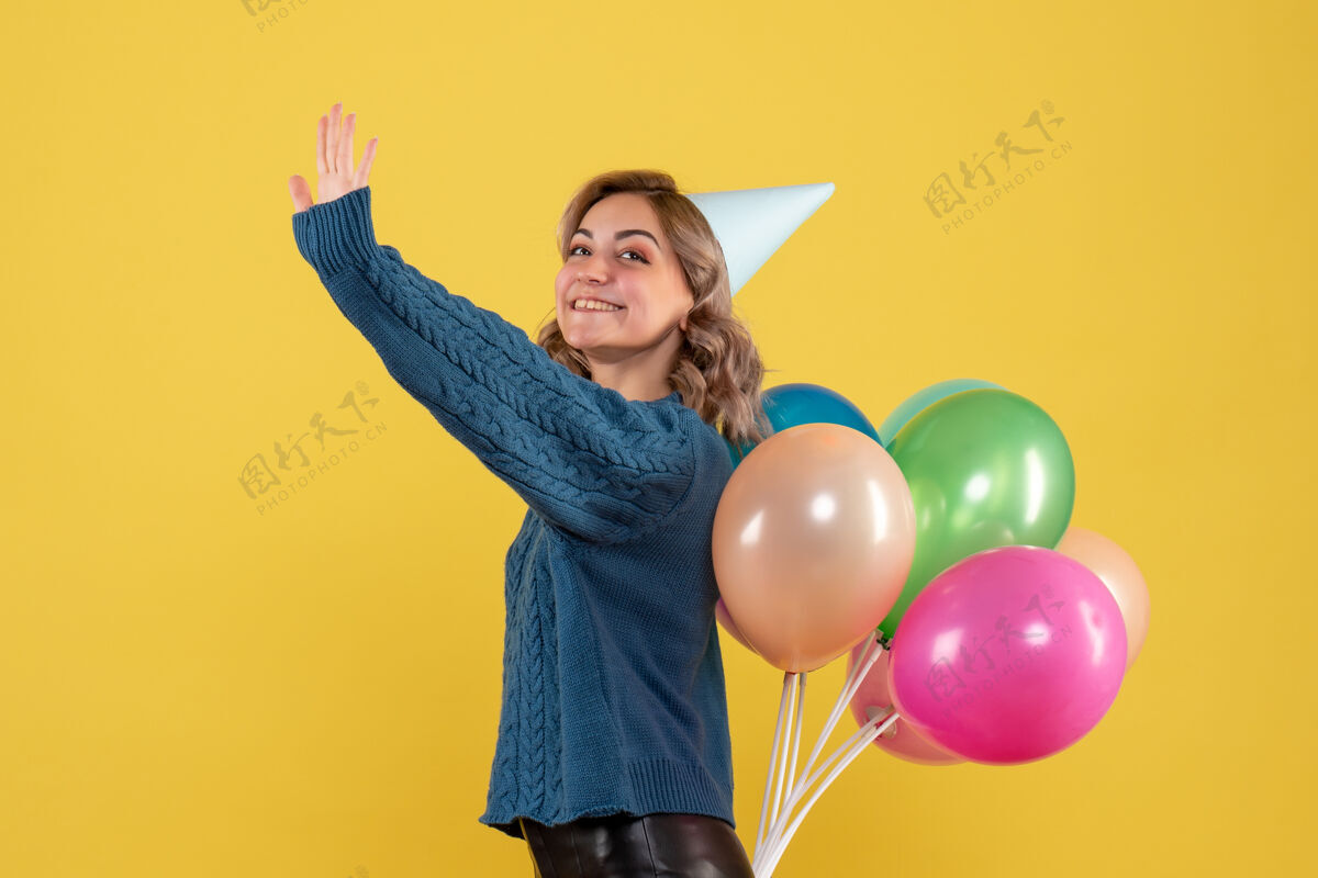 背面年轻的女性把五颜六色的气球藏在黄色的背上气球人生日