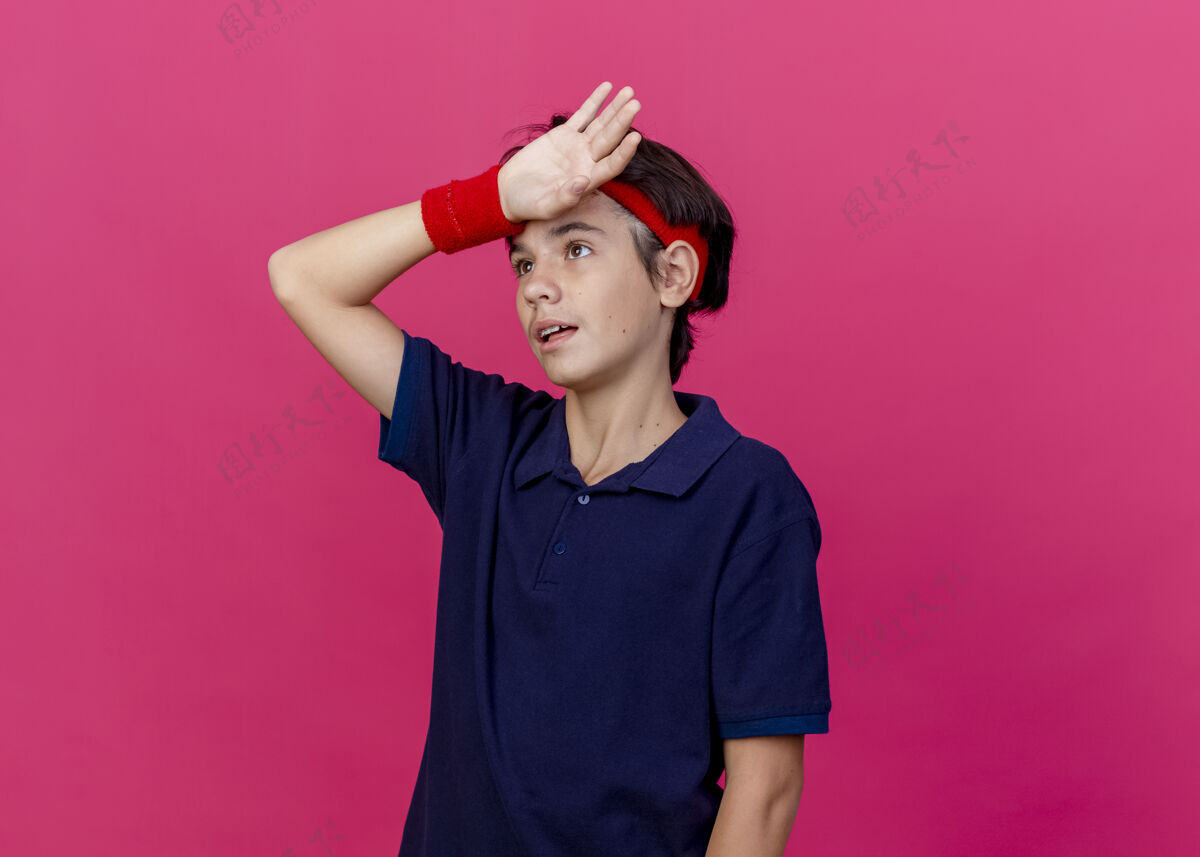 手疲惫的年轻英俊的运动男孩戴着头带和护腕 戴着牙套 手放在额头上 在深红色背景上孤立地向上看 还有复制空间年轻腕带头带
