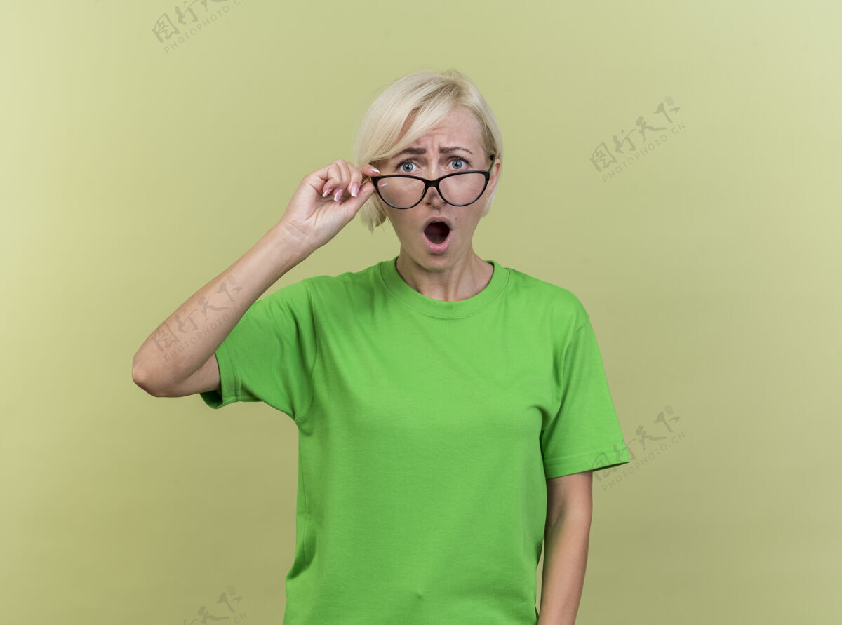 抢手惊讶的中年金发斯拉夫女人戴着眼镜抓住他们看相机孤立的橄榄绿背景与复制空间眼镜中年橄榄