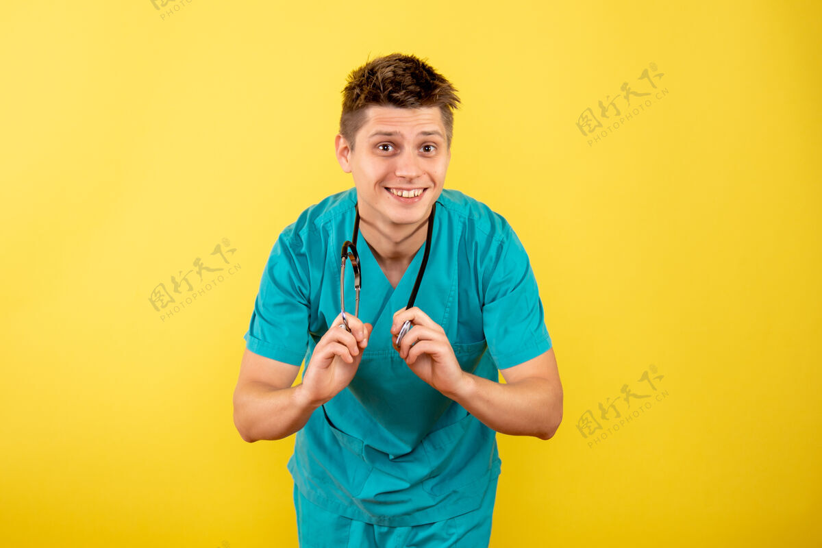 背景前视图年轻男性医生穿着医疗服 黄色背景上有听诊器医学西装听诊器