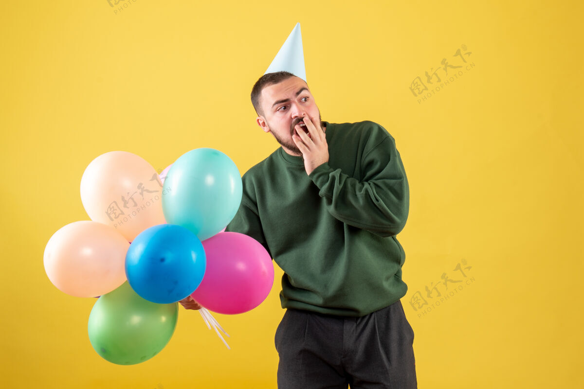 年轻的男性正面图黄色背景上有彩色气球的年轻男性气球乐趣购物