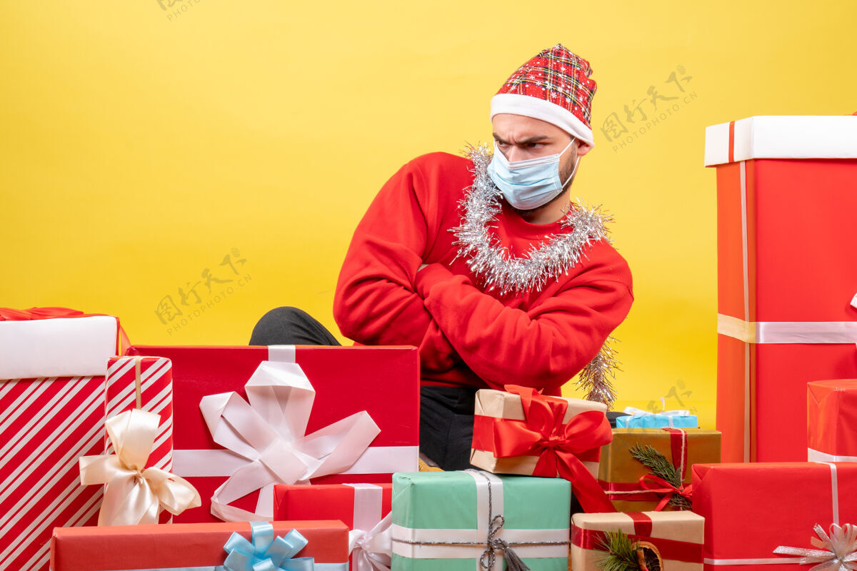 圣诞节正面图：坐在黄色背景上的年轻男性礼物礼物帽子背景