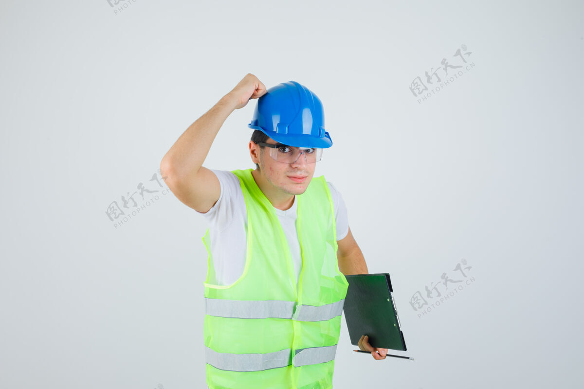 头盔小男孩拿着写字板和笔 手放在头盔上 穿着施工制服 表情严肃 正对着前方休闲时尚青少年