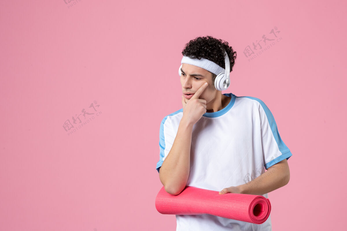 微笑正面图穿着运动服的年轻男性 粉色墙上有瑜伽垫粉色正面盒子