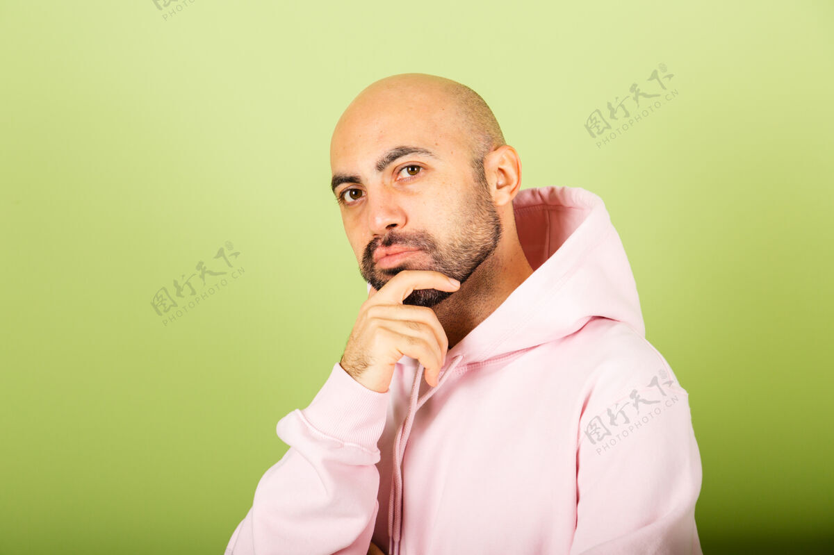 站立年轻秃顶的白人男子穿着粉色连帽衫 孤立无援 担心一个问题 担心和紧张的手放在下巴上快乐成人思考