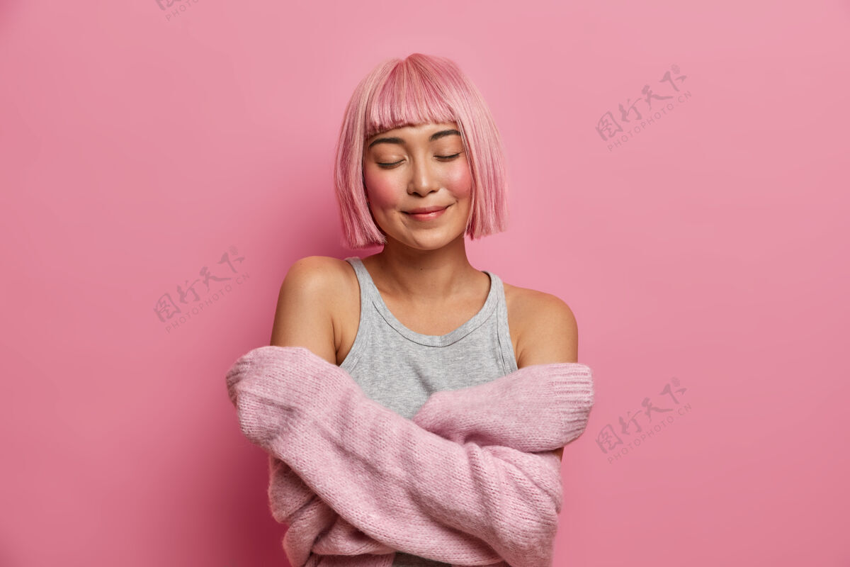 粉色假发女人 温柔 舒适高兴的粉红头发的亚洲女人拥抱自己 闭上眼睛 穿着柔软的毛衣感到舒适 站起来时尚亚洲人模特