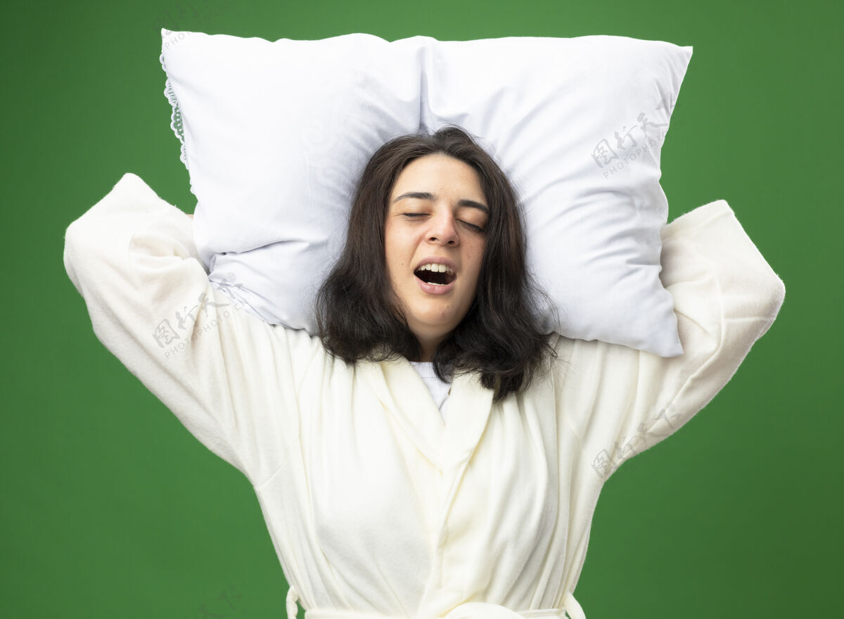 女孩疼痛的年轻白种人生病的女孩穿着长袍抱着枕头在头下尖叫闭上眼睛隔离在绿色背景眼睛枕头疾病