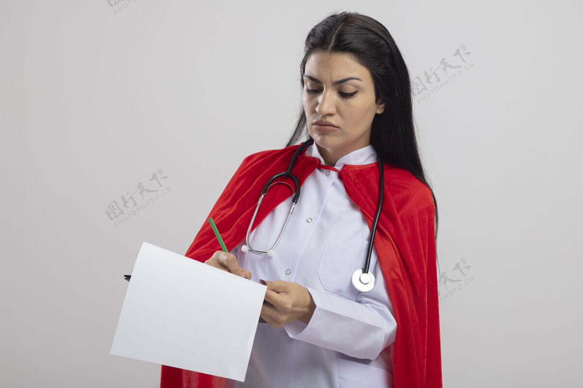 皱眉愁眉不展的年轻白种人超级英雄女孩戴着听诊器拿着剪贴板用铅笔在上面写字 白色背景上有空白穿铅笔白色