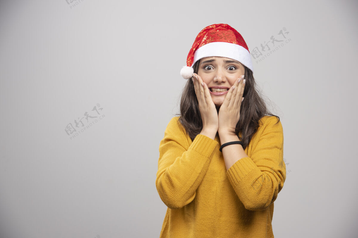 人戴着圣诞老人红帽子的年轻女子在白墙上摆姿势女士年轻礼品盒
