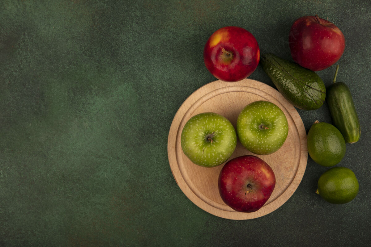 黄瓜木制厨房板上美味的红苹果和绿苹果的俯视图 绿色墙壁上隔离着酸橙 鳄梨和黄瓜 还有复印空间农业中心苹果