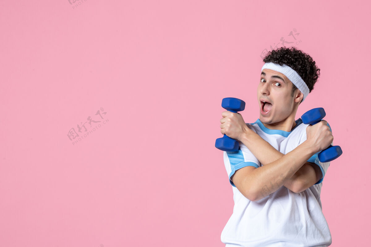 健身房正面图穿着运动服的年轻男性在粉色墙上用哑铃锻炼视野年轻男性微笑