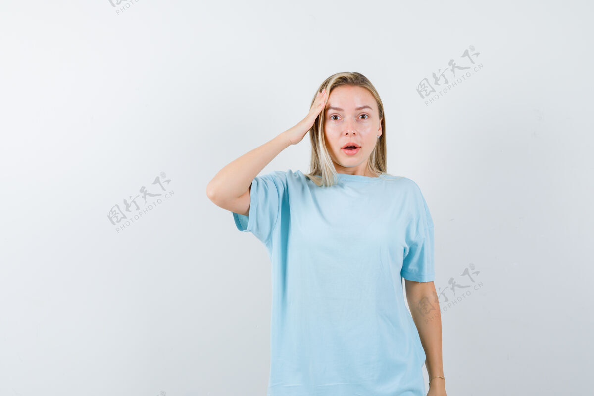 模特金发女孩手牵手在太阳穴上 穿着蓝色t恤 看起来很惊讶前视图肖像漂亮快乐