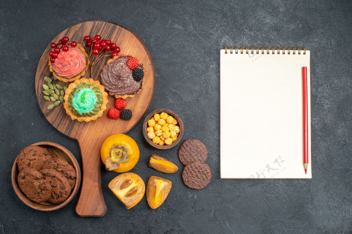 笔记本俯瞰美味的蛋糕与饼干和水果在黑暗的桌子上甜甜的馅饼蛋糕健康甜点餐