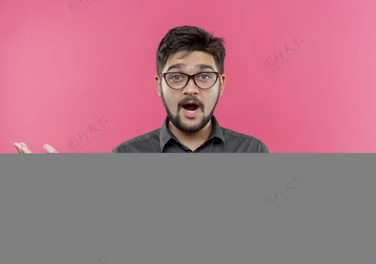 穿困惑的年轻商人戴着眼镜 把双手孤立在粉红色的墙上迷茫传年轻