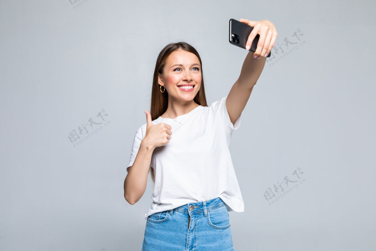 漂亮快乐开朗的年轻女子竖起大拇指在智能手机上自拍手机人拇指