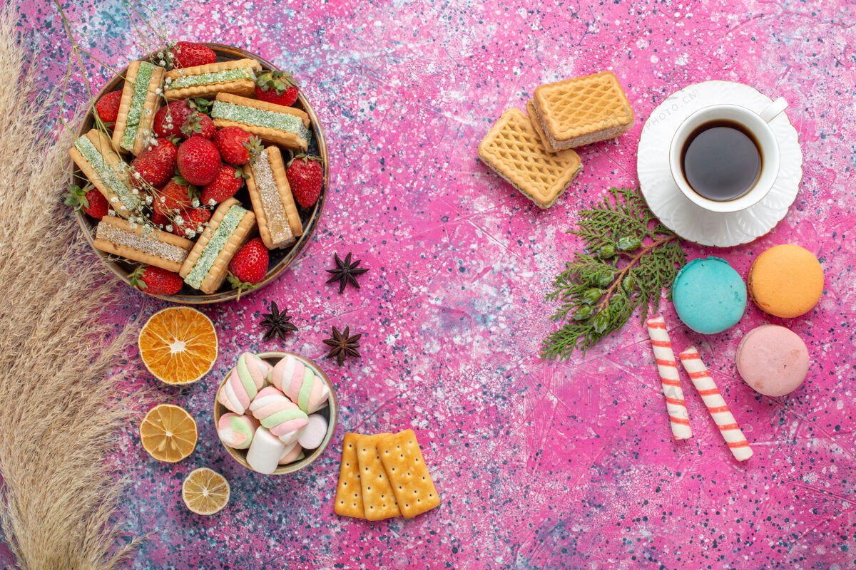 生的俯瞰美味的华夫饼干 粉色表面有法国马卡龙和新鲜的红色草莓早餐糖果草莓