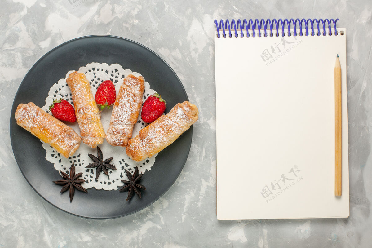 早餐糖粉百吉饼的俯视图美味的面团 白色表面上有草莓和记事本百吉饼顶视图食物