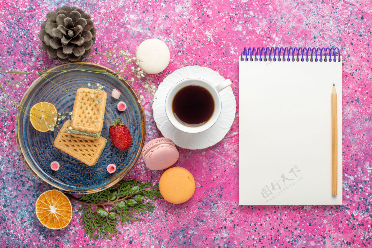 饼干美味的华夫饼与法国马卡龙和粉红色表面上的茶俯瞰图杯子法国顶视图