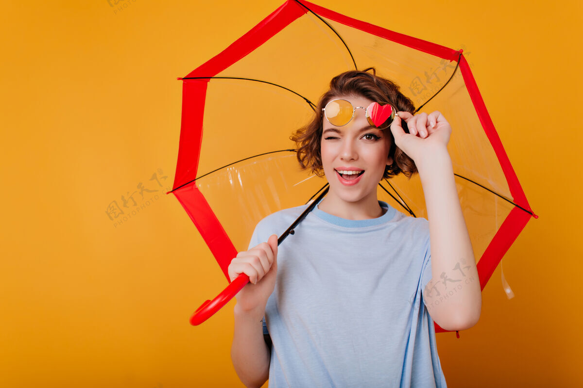 微笑迷人的戴眼镜的年轻女士在与伞的合影中玩得很开心可爱的卷发女孩和阳伞合影的摄影棚照片快乐游戏爱