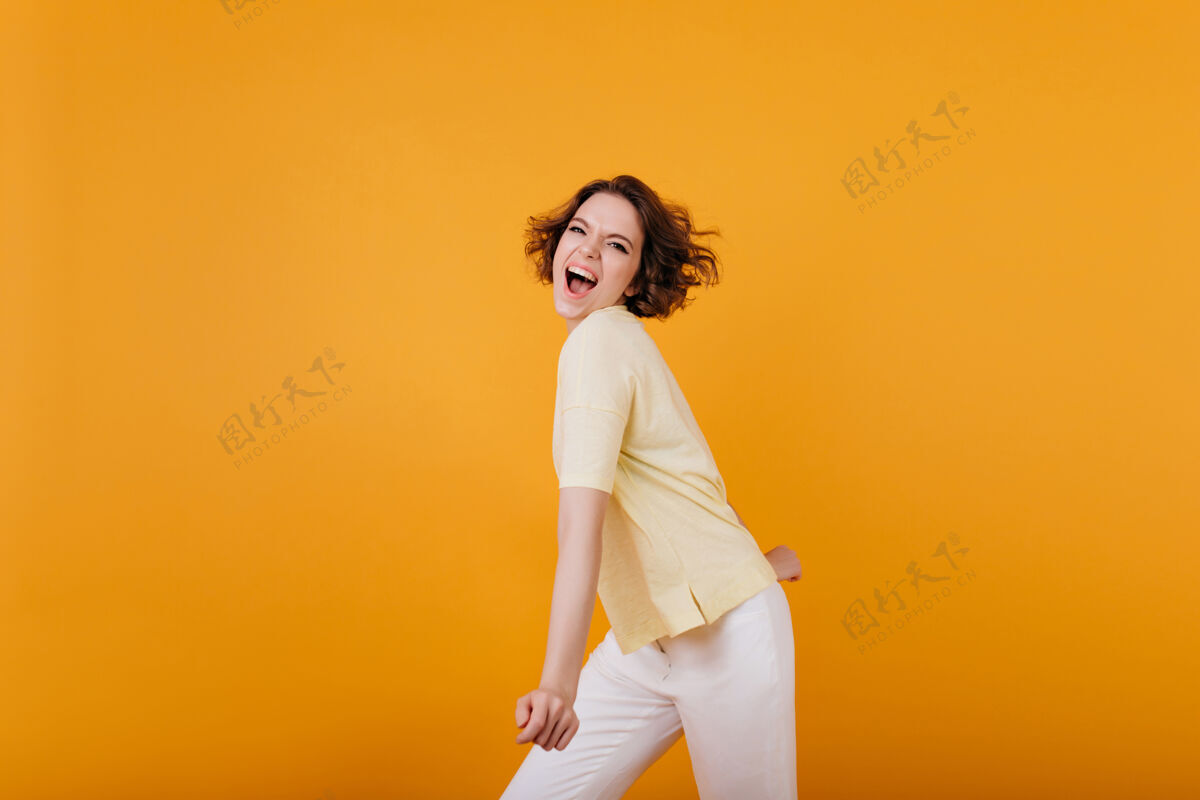 成人活泼的女孩 时尚的发型 在明亮的橙色墙上跳舞迷人的卷发女士 穿着浅黄色t恤 在室内玩得很开心活跃卷曲积极
