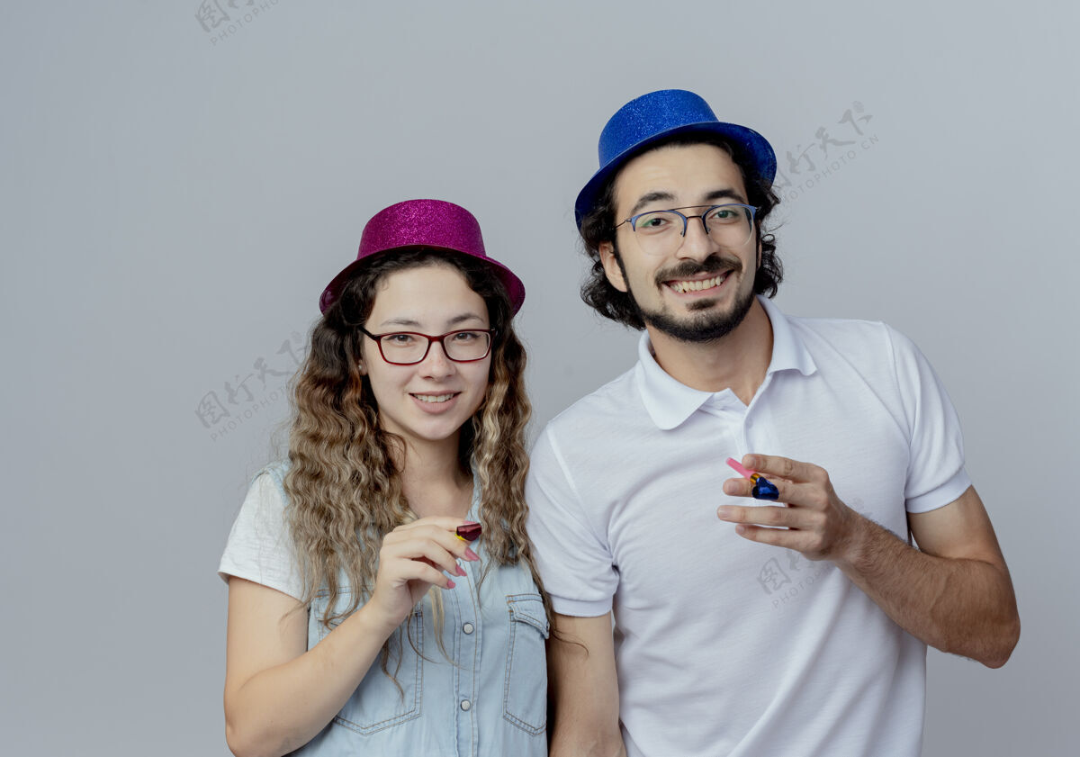 情侣微笑的年轻夫妇戴着生日帽 举着白色的口哨微笑年轻生日