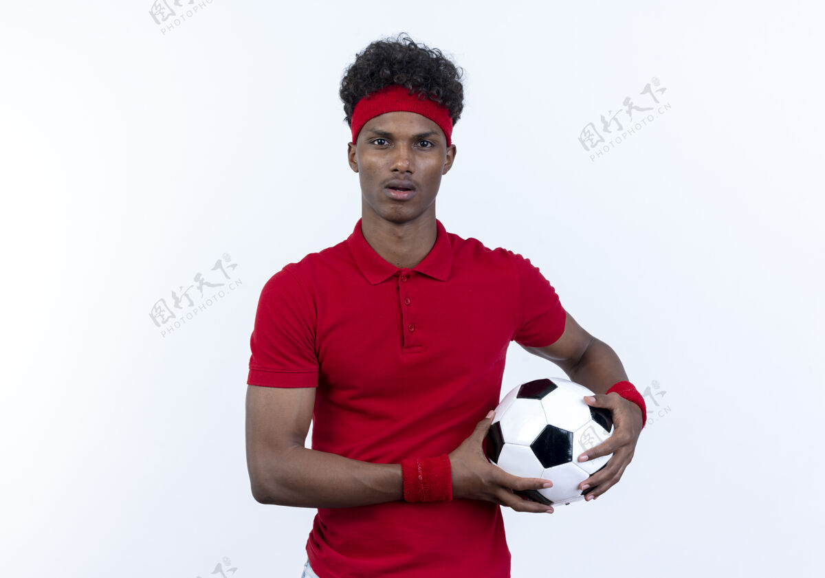 表情惊讶的年轻黑人美国运动男子戴着头带和手环举行的白色孤立的球男球手势