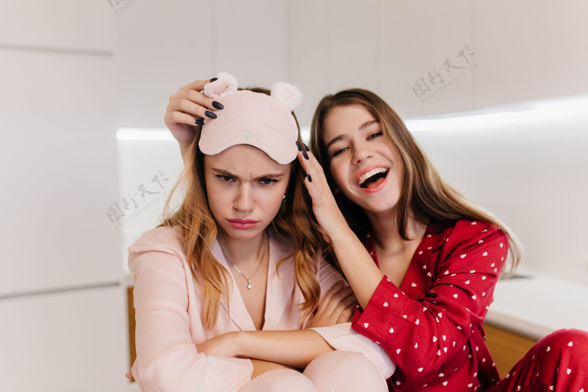 快乐一个戴着粉红色眼罩 双臂交叉在厨房里摆姿势的女人穿着红色睡衣的白人女孩在早晨笑的室内照片眼罩睡衣青少年