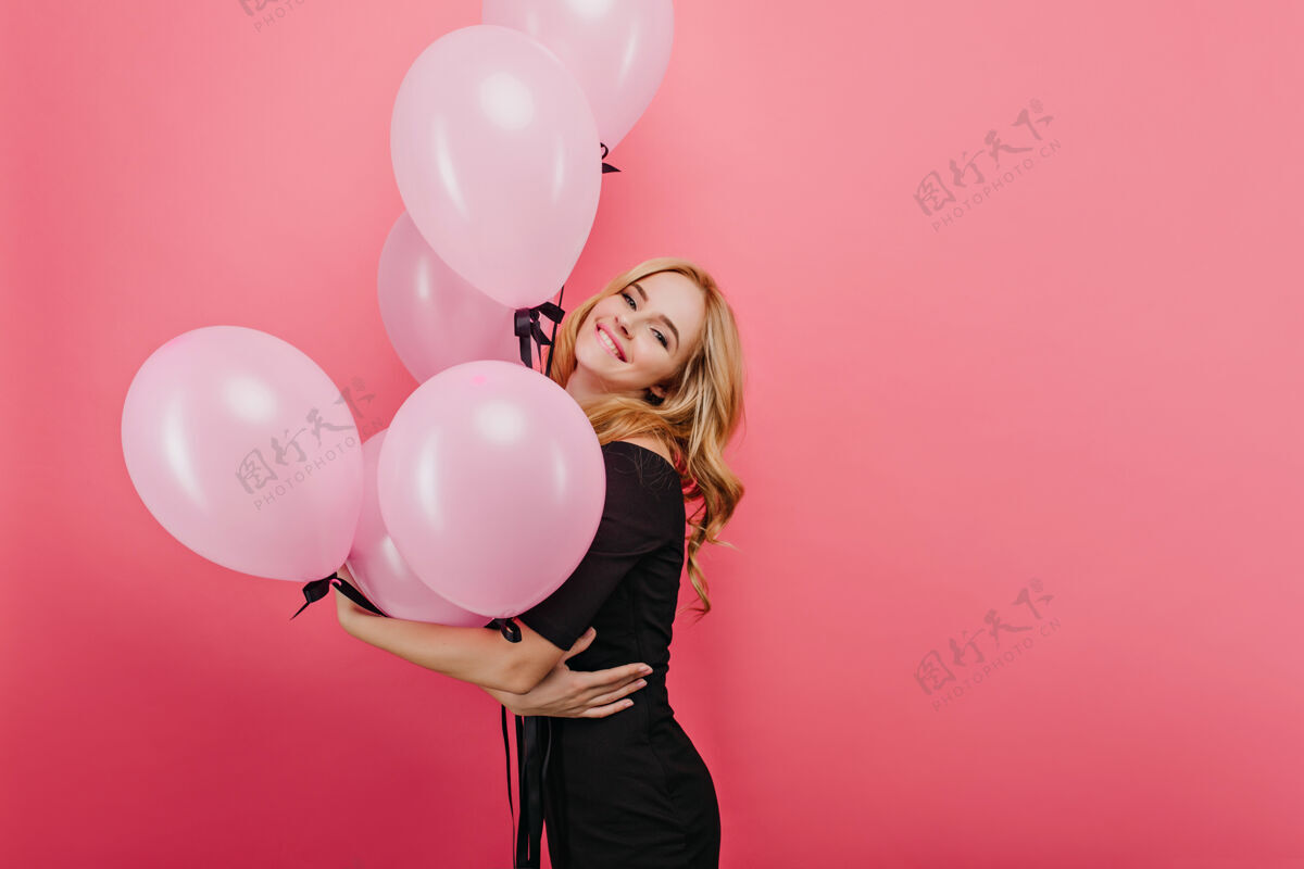 女人一位金发碧眼的年轻女子在明亮的墙上微笑着摆姿势室内照片是一位高兴的欧洲生日女孩手持气球表情肖像成人