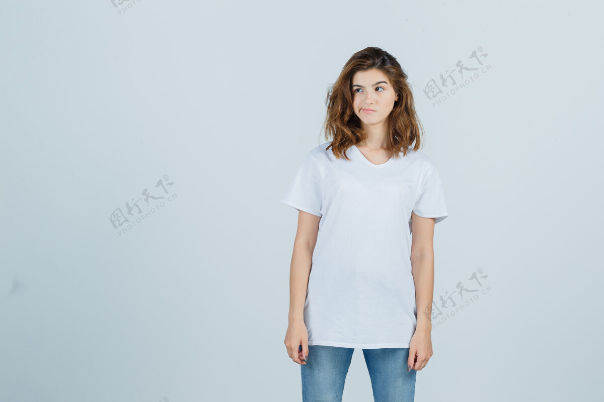 微笑年轻女孩的画像 一边看 弯曲的嘴唇在白色t恤和期待沉思的前视图模型旁白成人