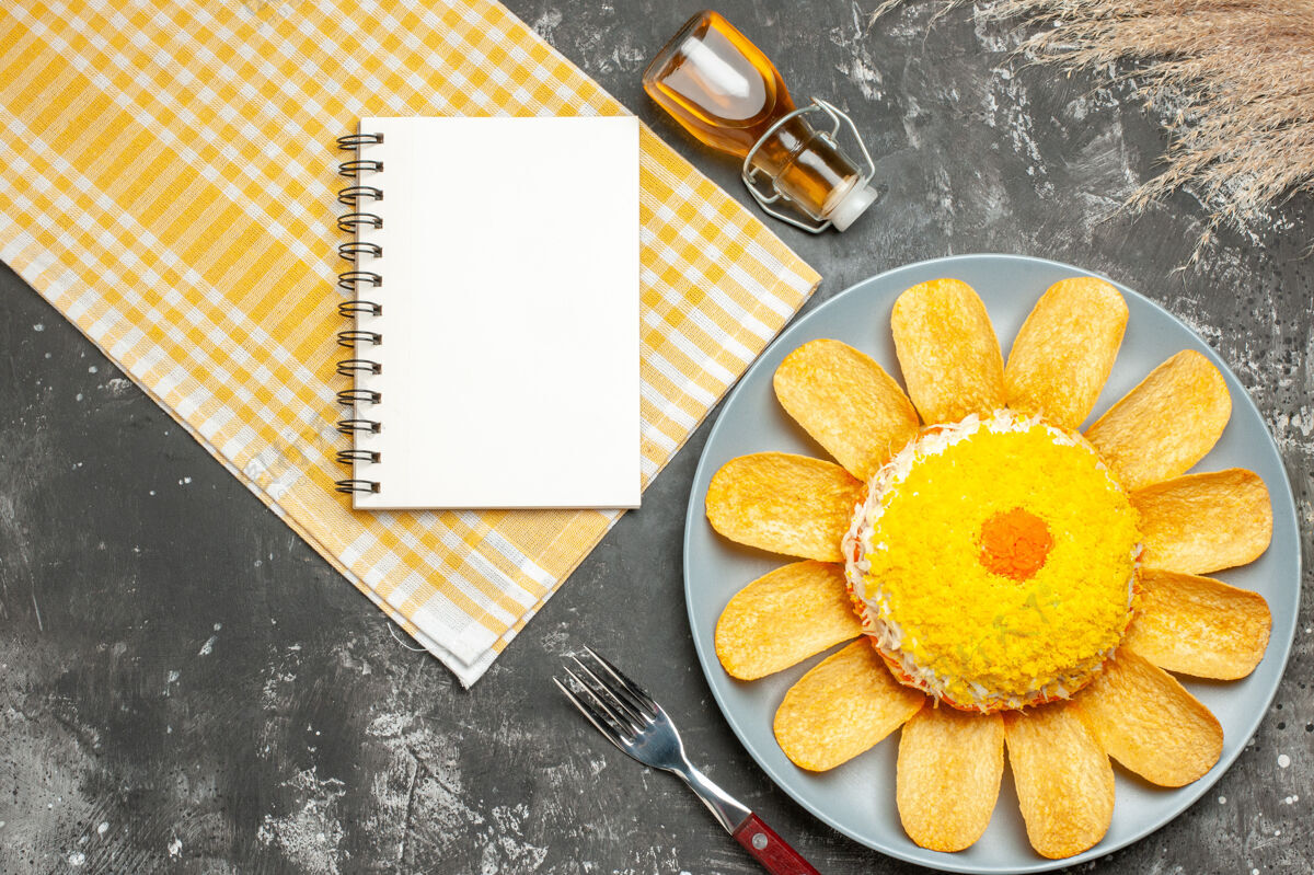 记事本沙拉的顶视图在右边 黄色餐巾纸 油瓶 叉子 小麦和记事本在深灰色的桌子上瓶子叉子壁板