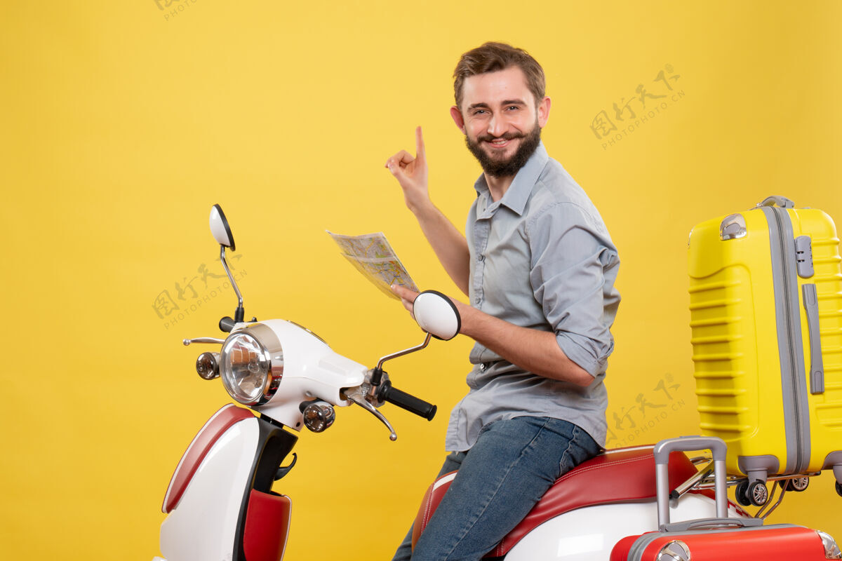 成人带着微笑的年轻人坐在摩托车上 提着手提箱 拿着黄色的地图 这是一个旅游概念持有旅游摩托车