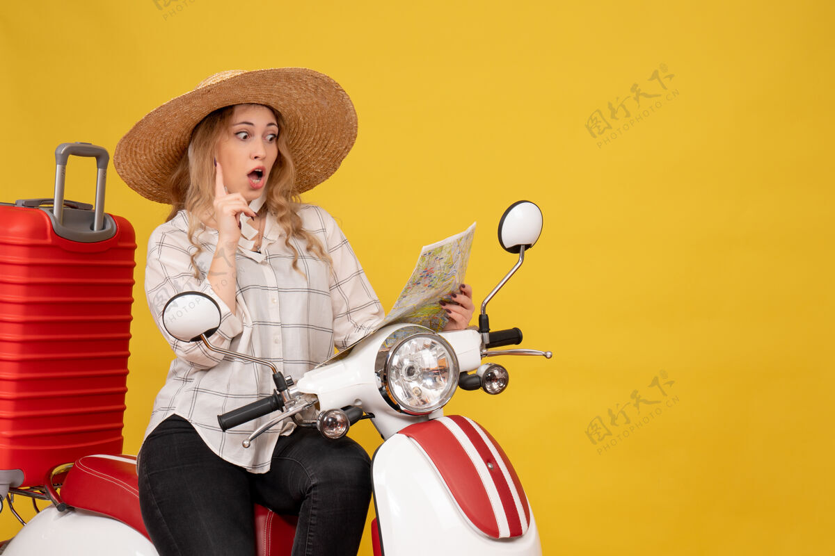 高尔夫球手俯视图是一个戴着帽子坐在摩托车上看着黄色地图的惊讶的年轻女子帽子肖像摩托车