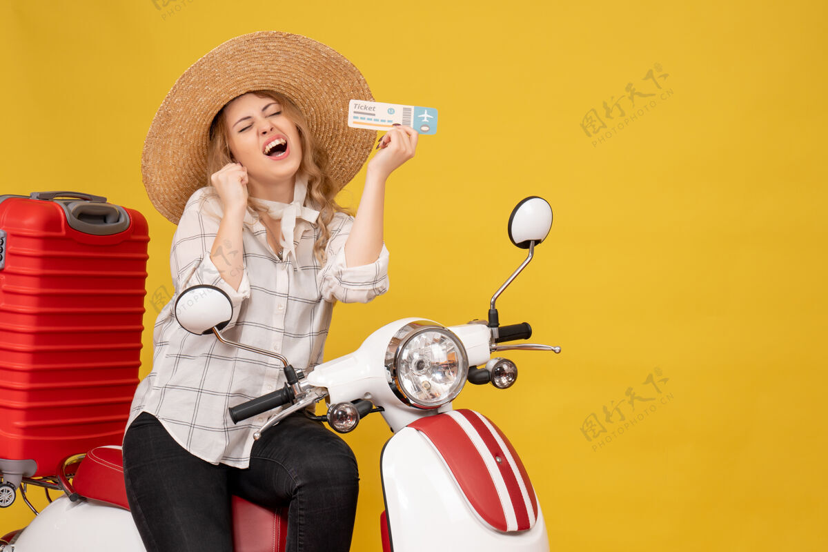 黑色戴着帽子 坐在摩托车上 拿着黄色的车票 心情愉快的年轻女子的俯视图年轻女子上衣手持