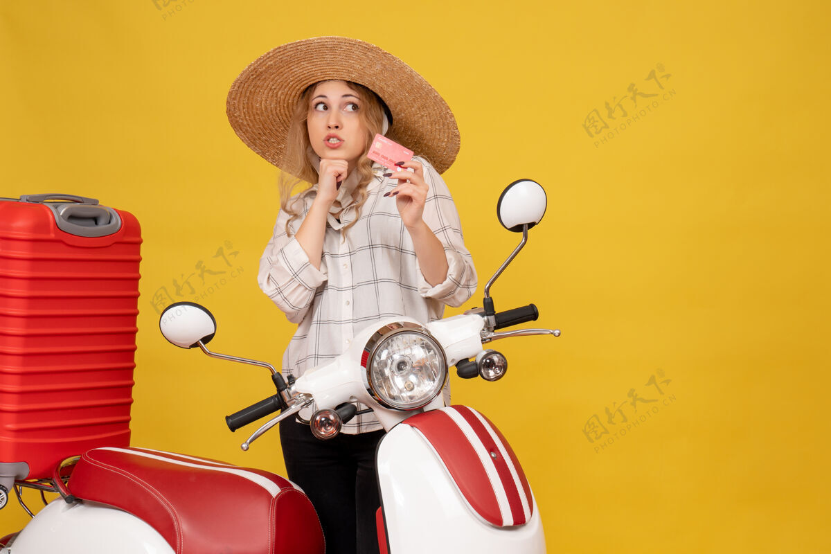 摩托车前视图是一个戴着帽子的年轻女子坐在摩托车上拿着银行卡 正在收拾行李人收集帽子