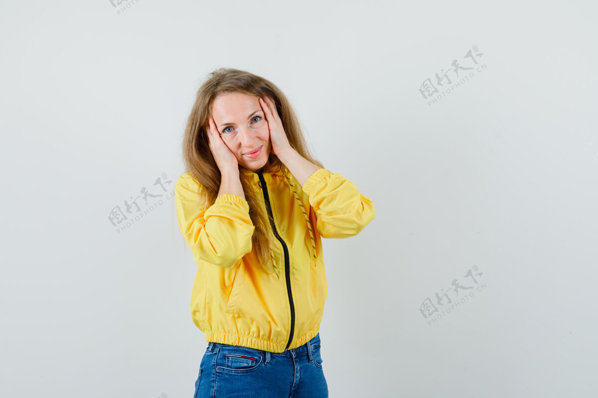 欢呼年轻女子手放在脸上 穿着黄色棒球服和蓝色牛仔裤 看起来很迷人 正面视图时尚女人年轻