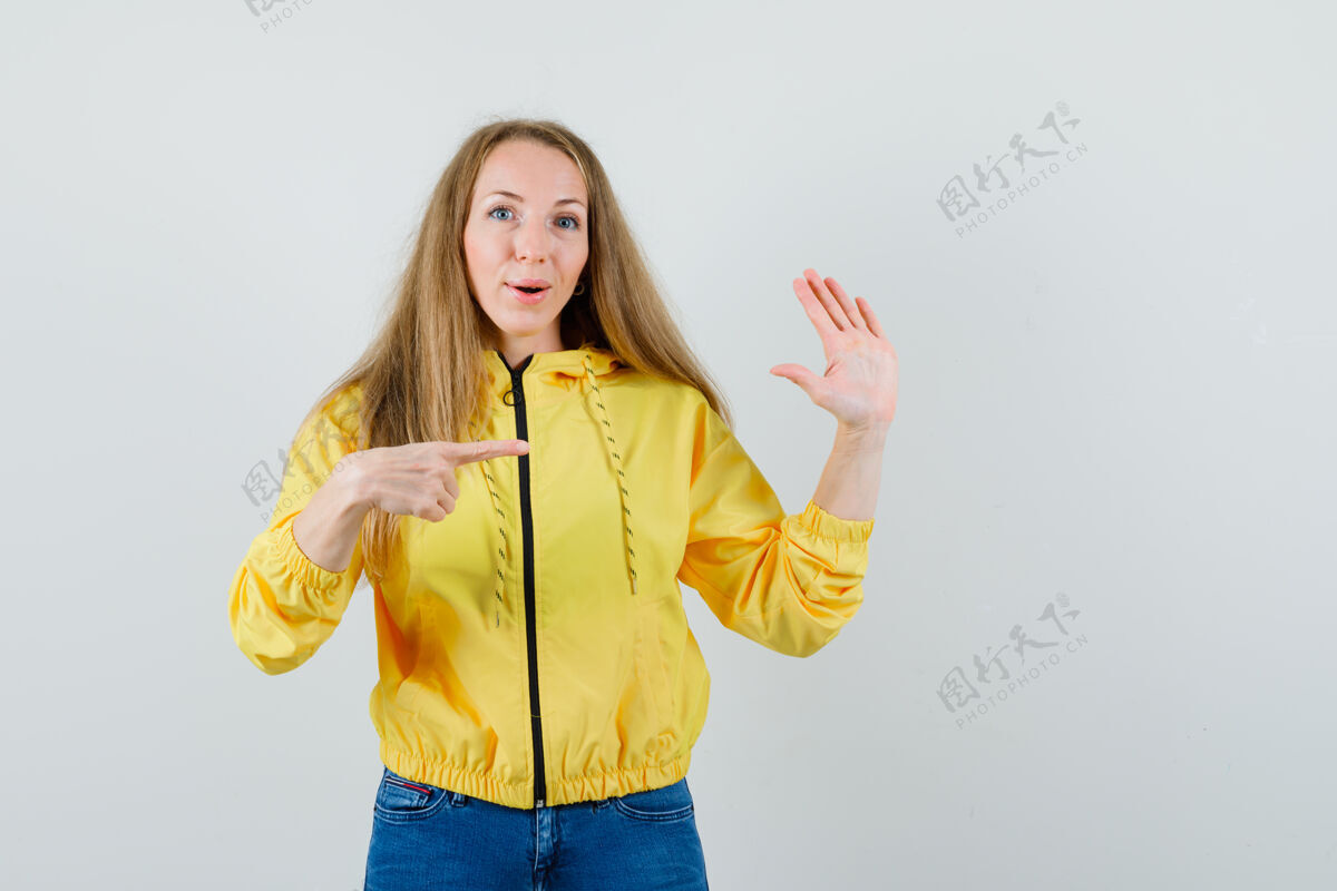 指向身穿黄色棒球服和蓝色牛仔裤的年轻女子 一只手指着停车标志 看上去很乐观 正对着前方时尚成人漂亮